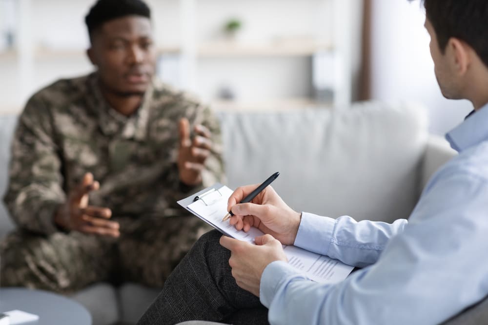 Psychologist taking notes while having conversation with black soldier